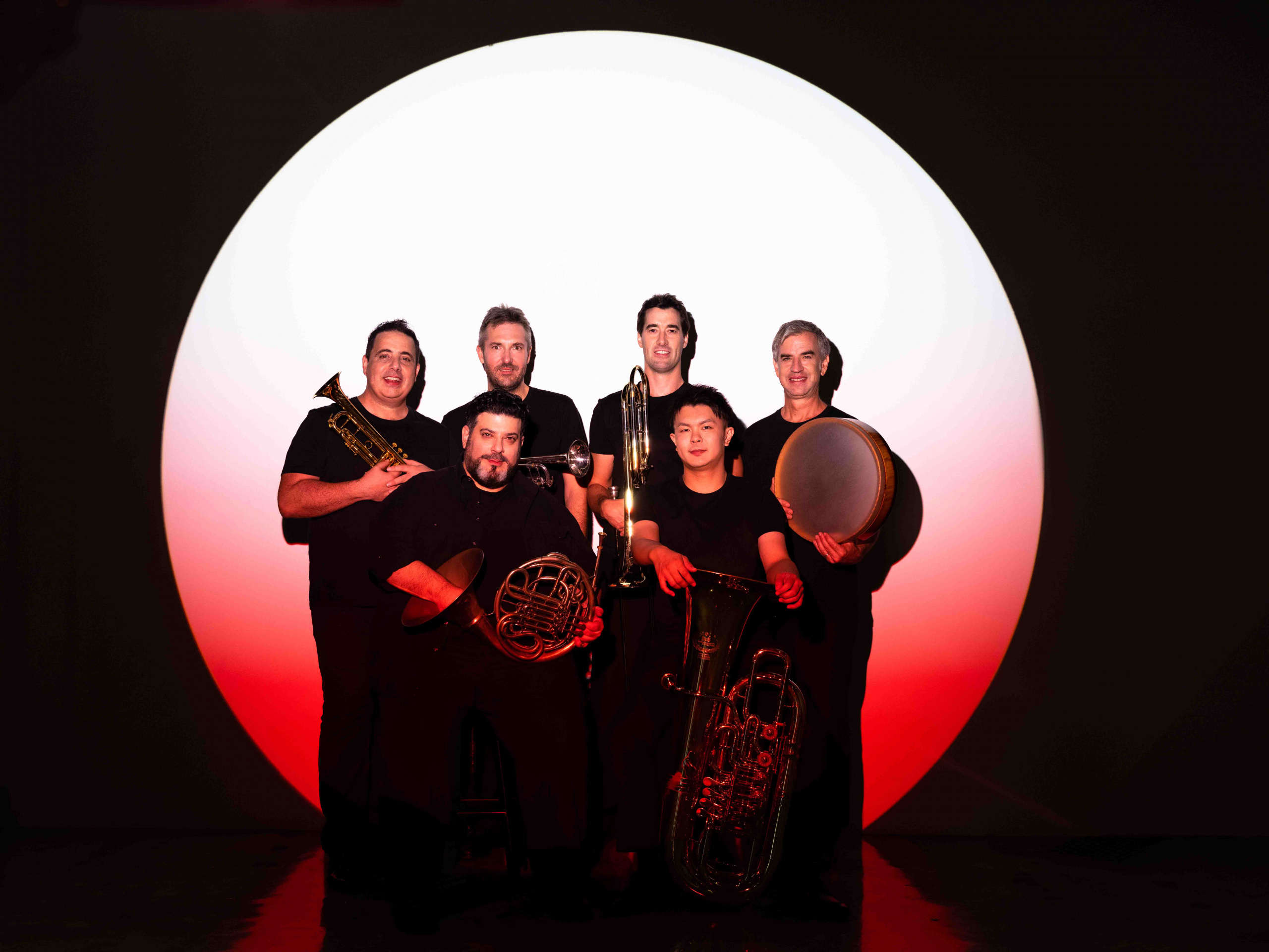 group shot of band members with their instruments against a white circle backdrop, and shot with red lighting