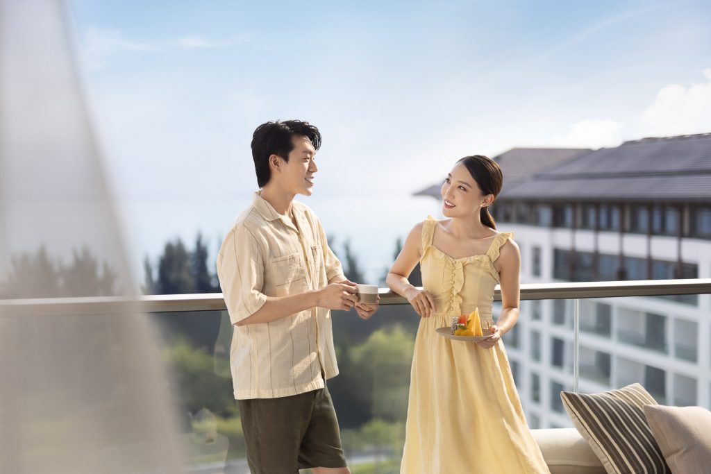 Hotel resort lifestyle photographer Hilton China Asia commercial - A couple is on the balcony of there hotel room, having some tea. We can see the sea behind them and trees.