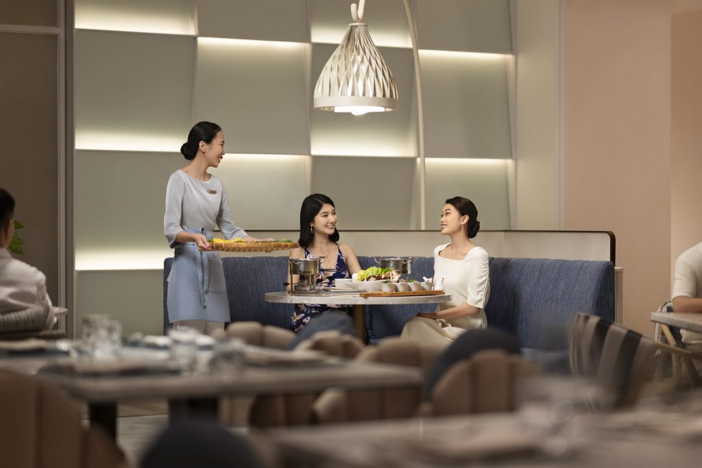 Hotel resort lifestyle photographer Hilton China Asia commercial - Two friends are having dinner in the hotel restaurant. The waitress brings them food on a tray